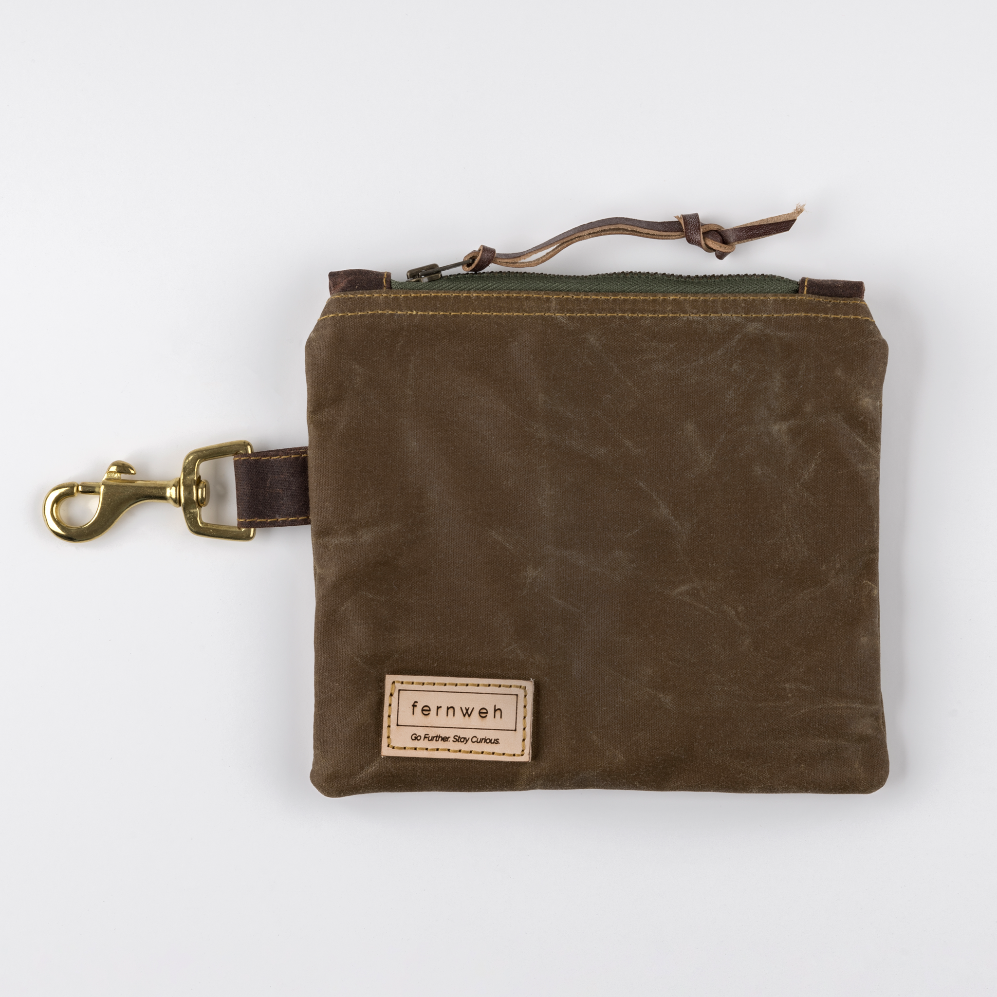 Image shows a Fernweh UK waxed cotton pouch in a brown shade, with a green zip. The pouch is on a white background and features a solid brass clip.