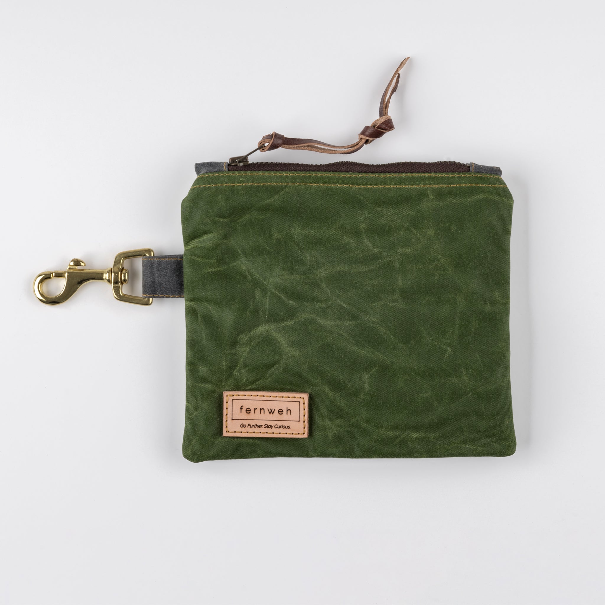 Image shows a moss green waxed cotton canvas pouch, sitting on a white background. The pouch has a solid bras clip on the left hand side 