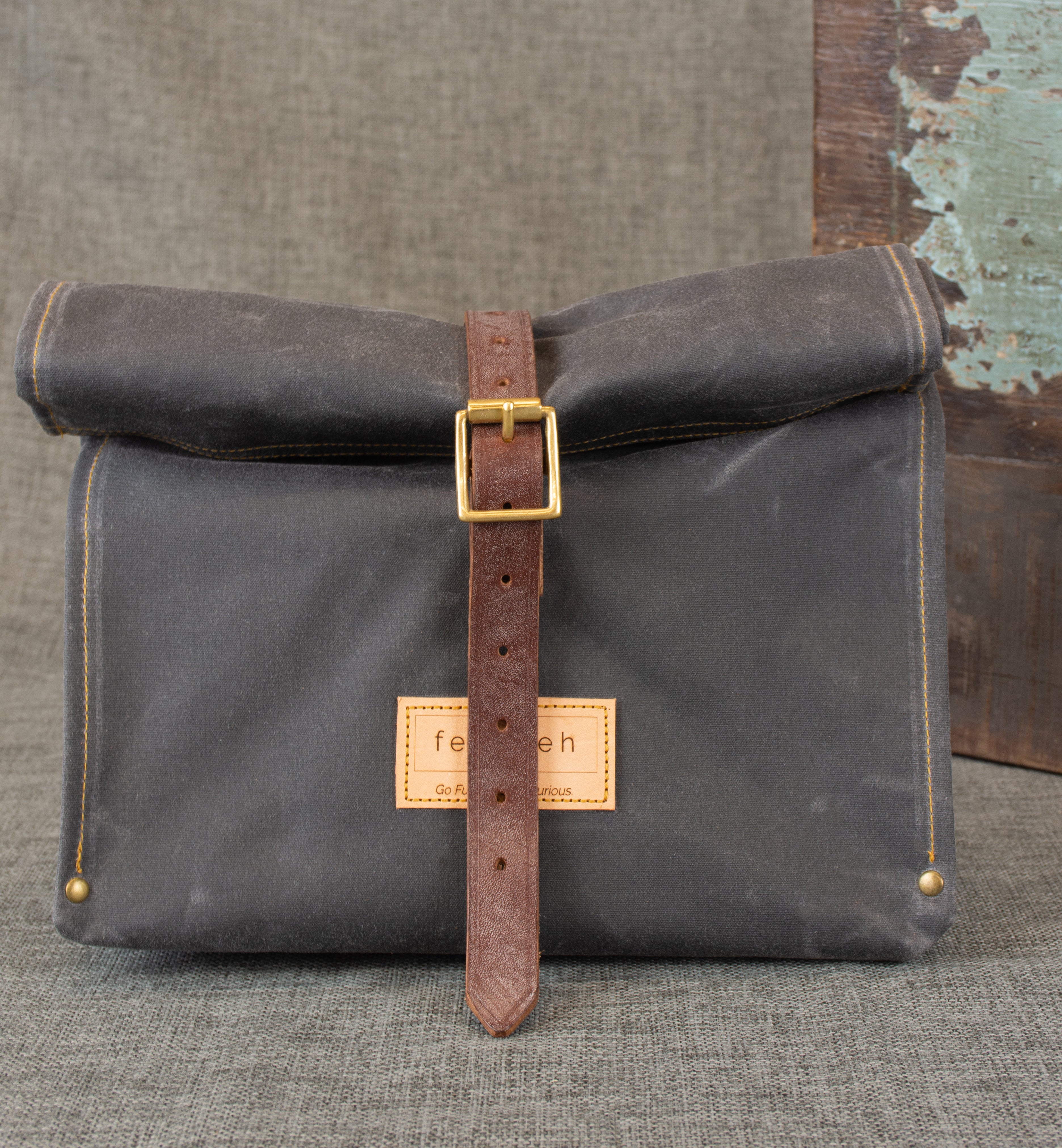 Image shows grey waxed cotton roll top bag with a brown oak bark tanned leather strap